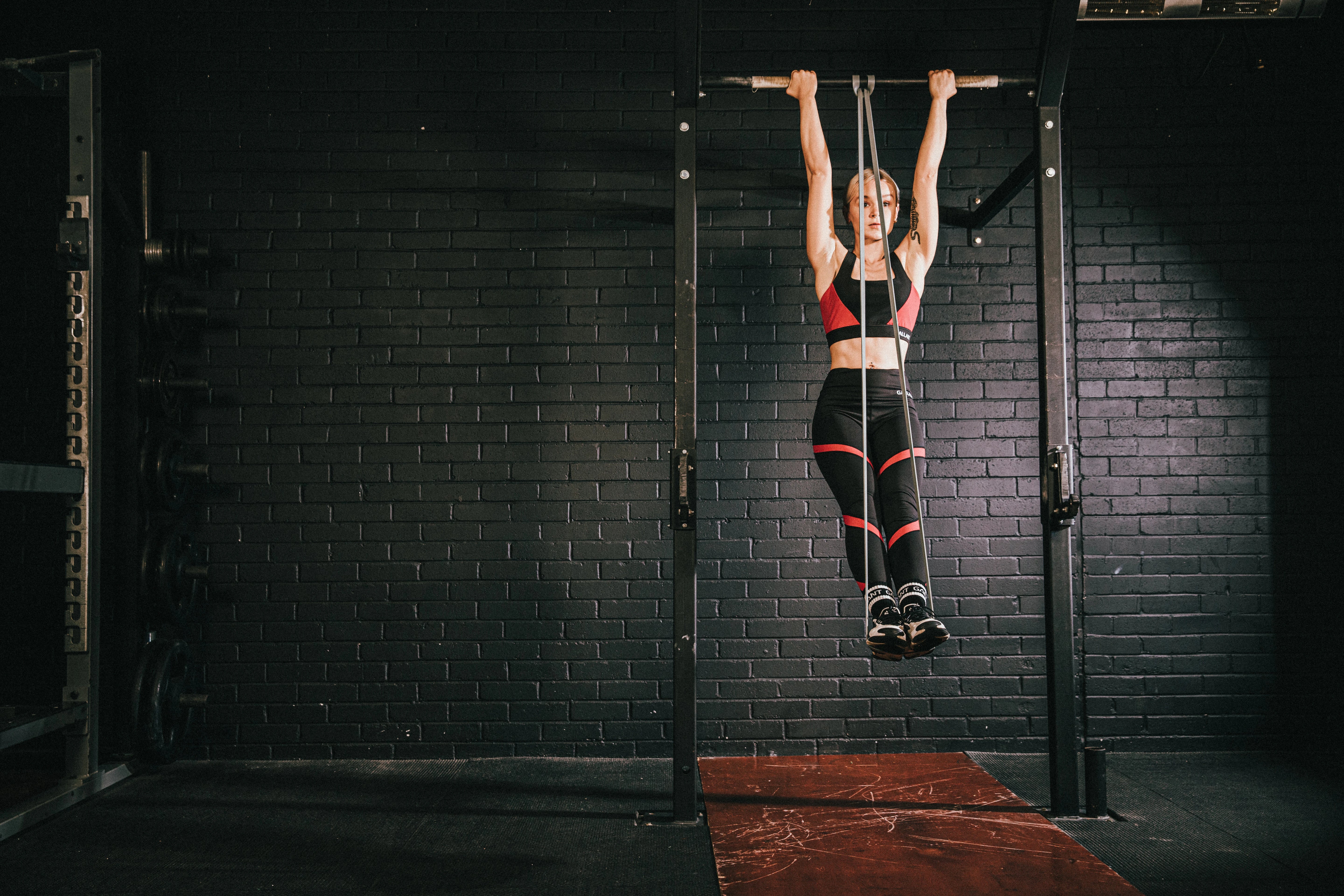 Person hanging from a pull-up bar in a gym with a dark brick wall background